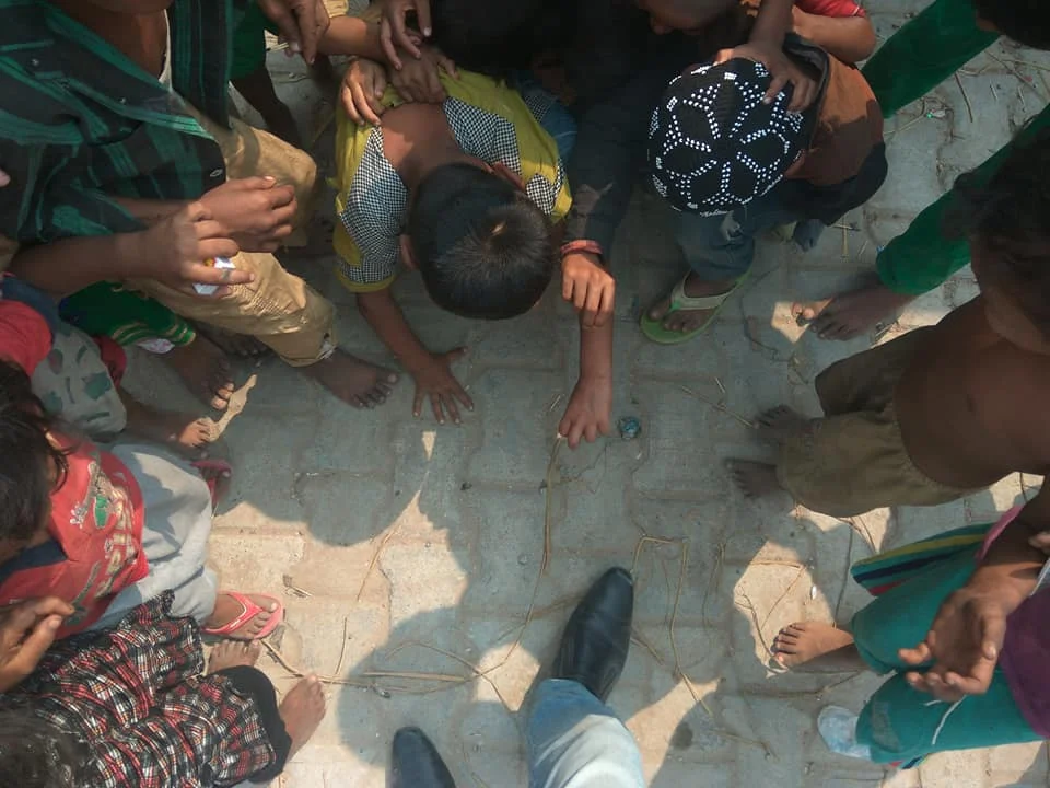 Children playing marbles on ground outdoors.