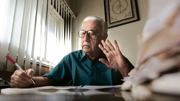 Elderly man writing and gesturing at home.