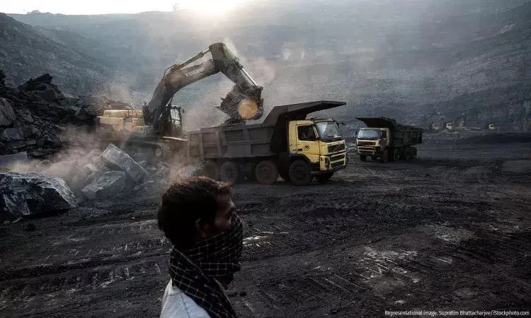 Man observing mining operations with trucks and excavator.