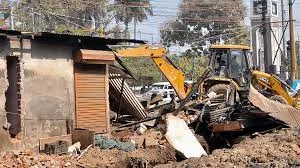 Excavator demolishing small building at construction site.