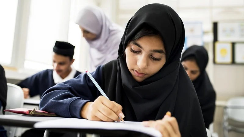 Student wearing hijab focused on writing in classroom.