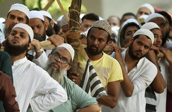 Group of men gathered outdoors, some wearing white caps.