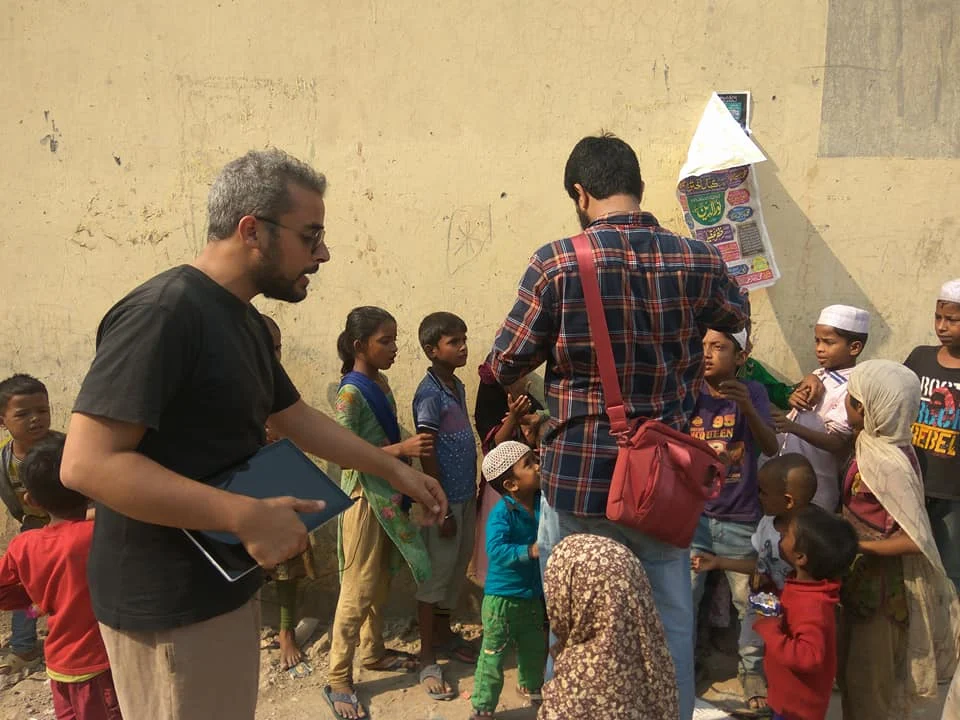 Men interacting with children outdoors near wall.