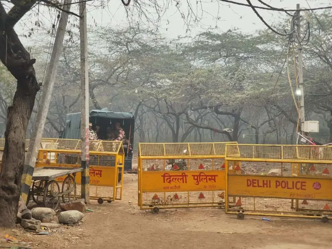 Delhi police barricades on dusty road with trees.