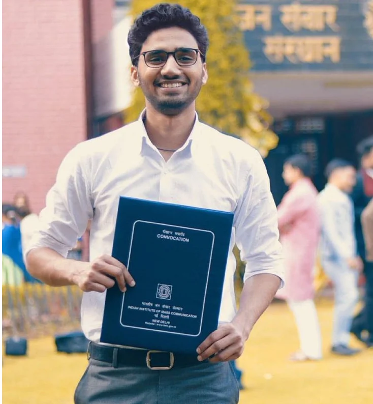 Graduate holding convocation folder, smiling outdoors.