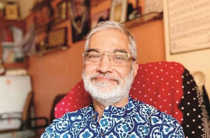 Smiling man with glasses in patterned blue shirt.