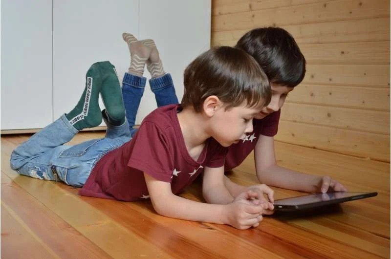 Two boys watching tablet on wooden floor.