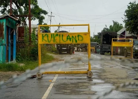 Yellow barrier with graffiti on a wet street.